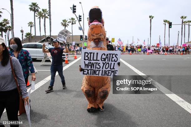 Protester wearing a dinosaur costume holds a placard that says Bill Gates Wants You Extinct Like Me during the demonstration. Citizens staged a...