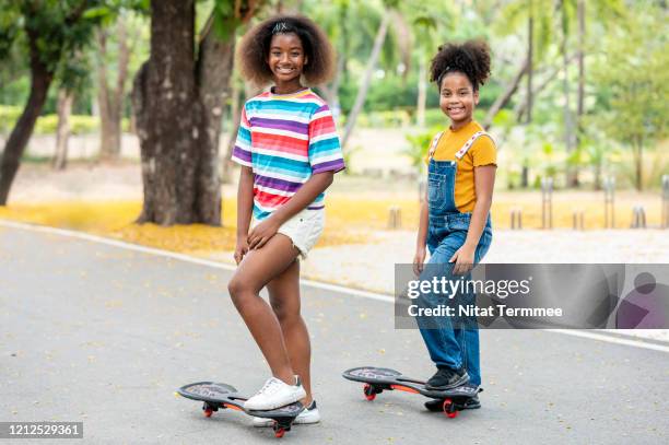 two young sisters african american skateboarding together in casual dress in the street and smiling happily. - 14 year old biracial girl curly hair stock pictures, royalty-free photos & images