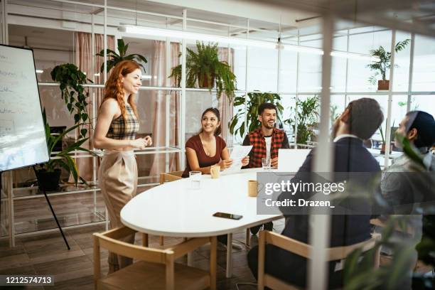 redhead latina presenta analisi ai colleghi in ufficio eco-friendly - riunione incontro sociale foto e immagini stock