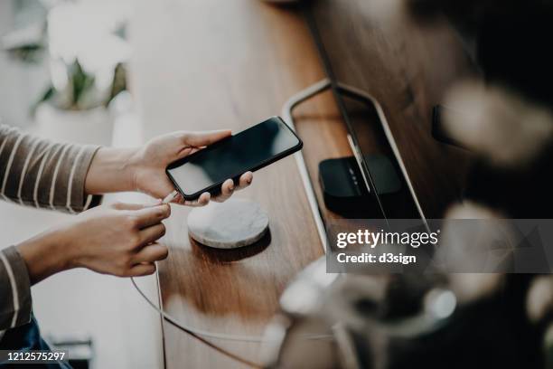 cropped shot of a woman's hand connecting smartphone to cable and getting charged / removing fully charged smartphone in the living room - power supply ストックフォトと画像