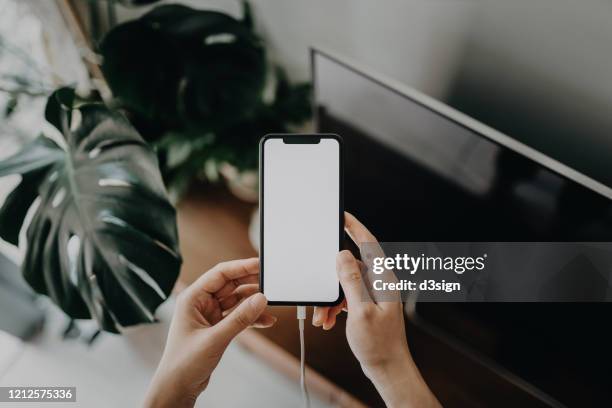 cropped shot of a woman's hand using smartphone while it is charging and connected to a power cable in the living room - usb cable stock pictures, royalty-free photos & images