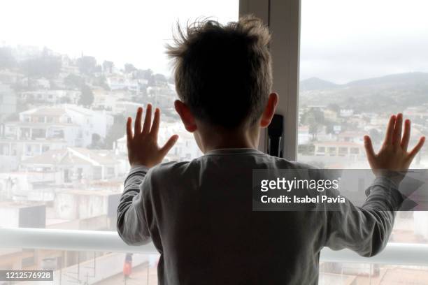 boy looking out of living room window - rear view hand window stockfoto's en -beelden