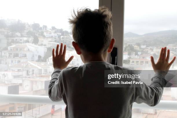 boy looking out of living room window - rear view hand window stock pictures, royalty-free photos & images