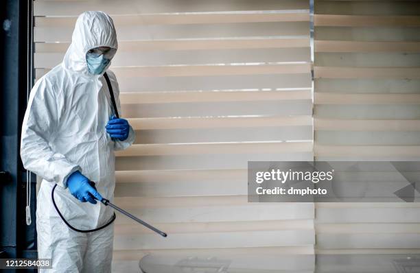 man in quarantine clothes disinfecting room - disinfection service stock pictures, royalty-free photos & images