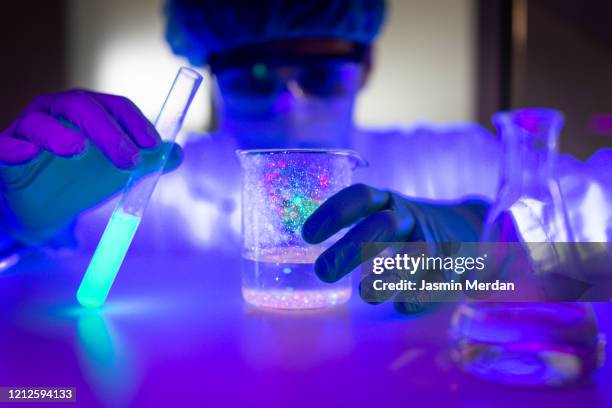 scientist observing lab tubes under ultraviolet light - doctor lab coat stockfoto's en -beelden