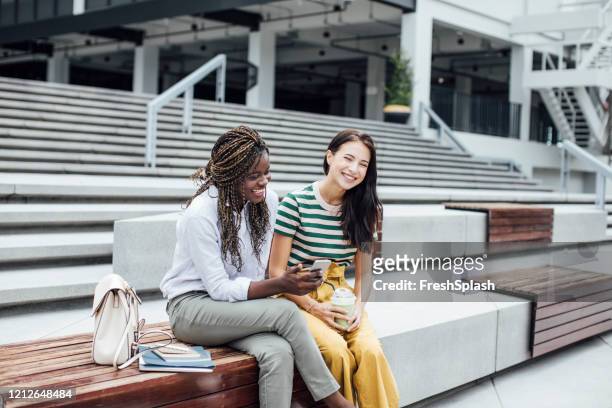 two female college students having a laugh while watching something on the smartphone - beautiful college girls stock pictures, royalty-free photos & images