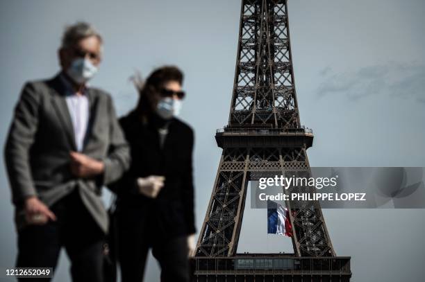 Man and a woman wearing face masks walk on Trocadero Plaza as a French national flag flies on the Eiffel Tower in background in Paris on May 11, 2020...