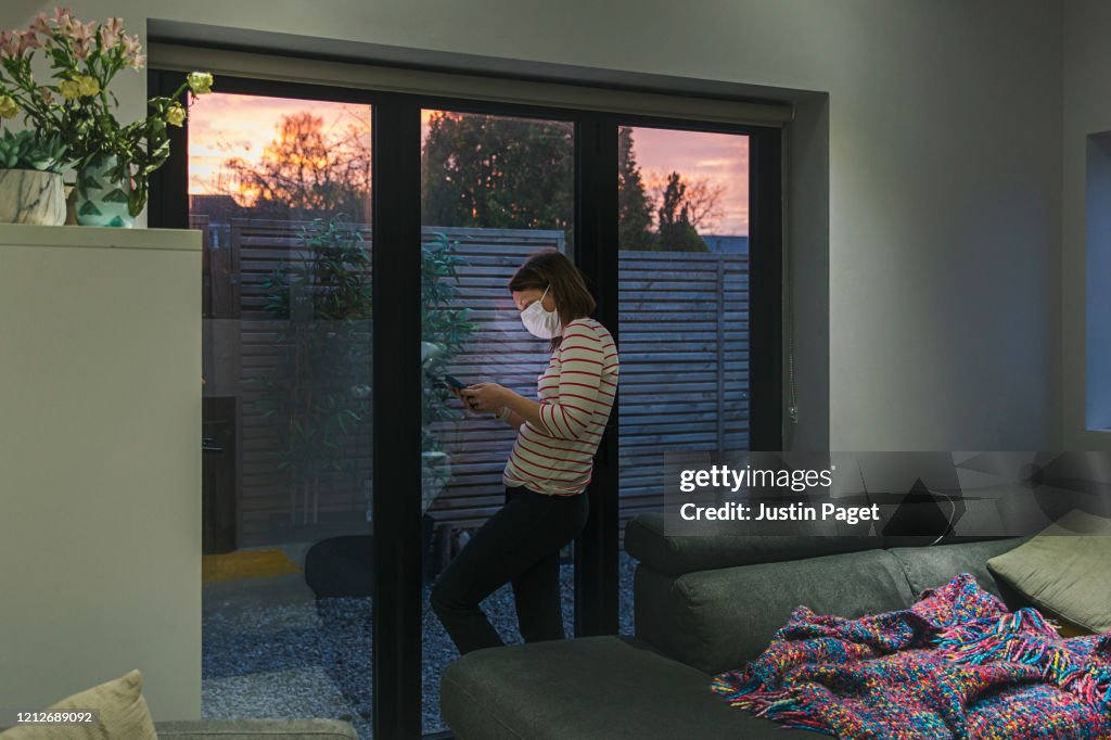 Woman in self isolation using smartphone by window