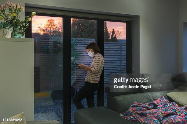 woman in self isolation using smartphone by window - quarantine stock pictures, royalty-free photos & images