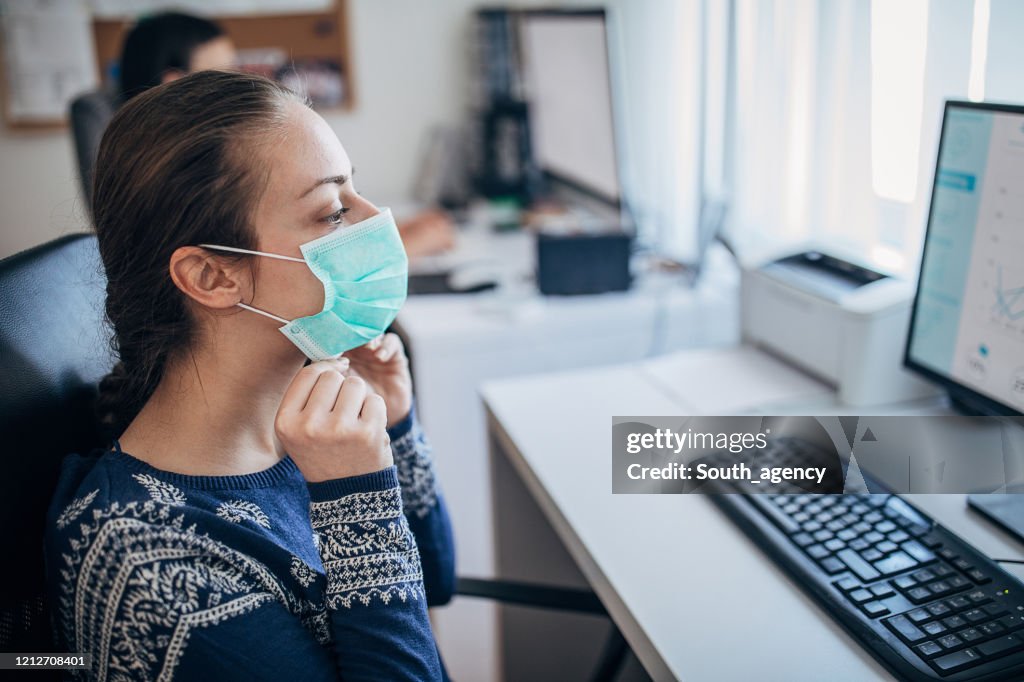 Mujer joven en la oficina poniéndose la máscara protectora, para evitar que el coronavirus se propague