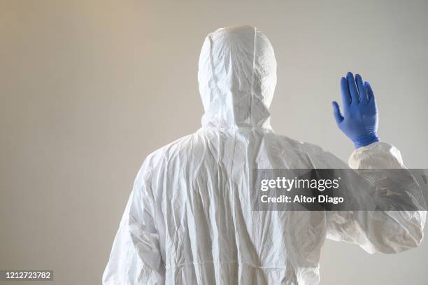 rear view of man with one hand up wearing gloves and protective suit (hazmat suit). coronavirus and other viruses concept. - protective suit stock pictures, royalty-free photos & images