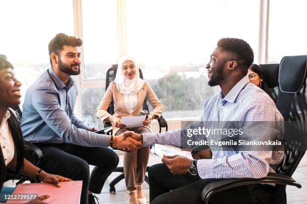 smiling black and indian businessmen handshaking after signing contract at multi-ethnic meeting. - islamic finance stock pictures, royalty-free photos & images