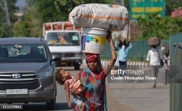 Migrant woman with a child and belongings on her head walks towards Madhya Pradesh from Gandhi Colony in Mansa Devi Complex on May 11, 2020 in...