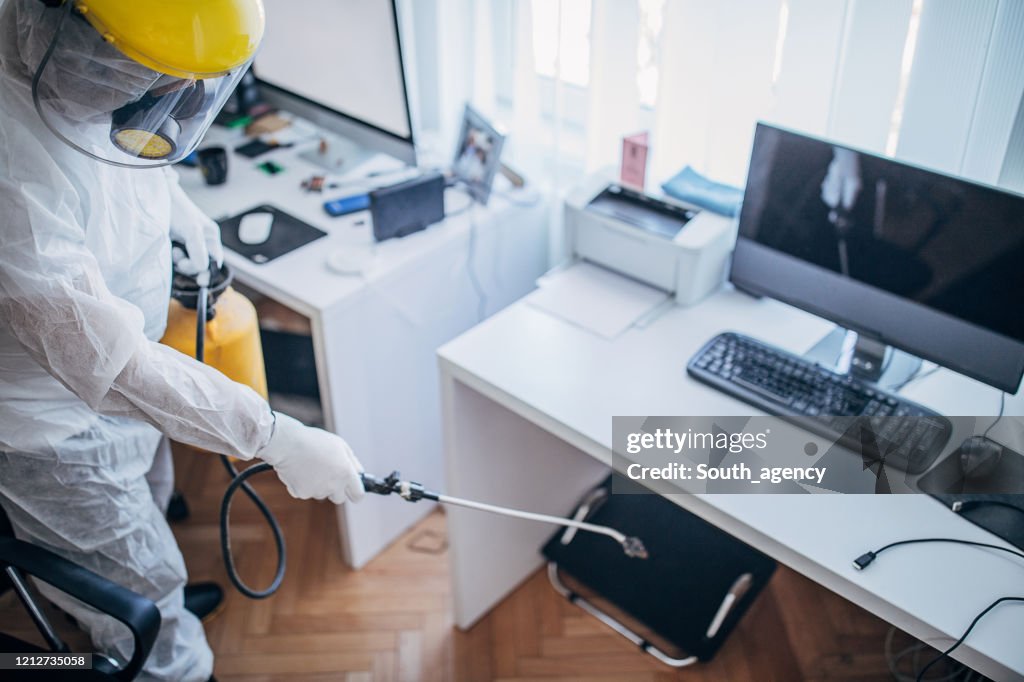 オフィスの仕事スペースを消毒する防護服を着た1人の男性
