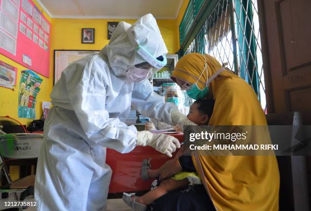 Nurses wearing protective gear give an injection of vaccine for measles to a child at a health centre in Palu on May 12, 2020. - As frontline...