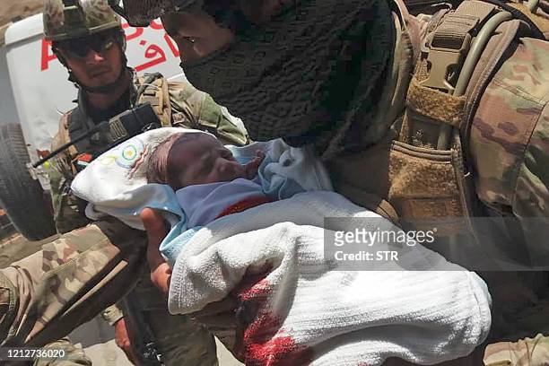 An Afghan security personnel carries a newborn baby from a hospital, at the site of an attack in Kabul on May 12, 2020. - Gunmen stormed a hospital...