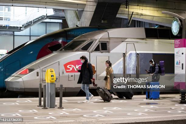 Travellers wearing protective mask walk next to a train past social distancing marks on the ground at the Gare Montparnasse train station in Paris on...