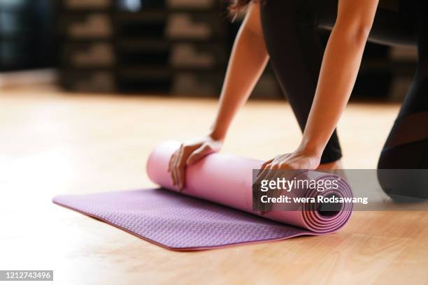 young woman folding yoga mat  after class end - salle yoga photos et images de collection