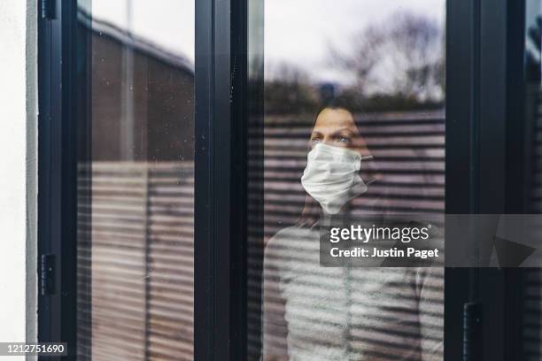 woman with mask looking out of window - quarantäne stock-fotos und bilder