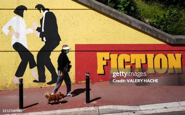 Woman wearing a face mask walks in front of a mural by Collectif Vertical Pulse of characters from Pulp Fiction, in a street in the French Riviera...