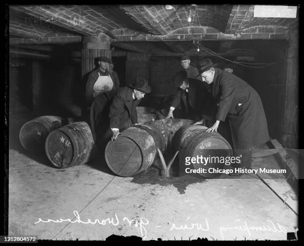 Group of men in a warehouse dumping wine from barrels into a hole in the ground during Prohibition, Chicago, Illinois, 1921.