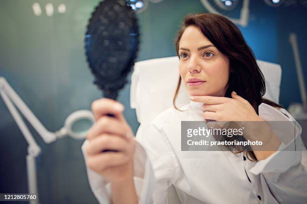 la giovane donna guarda il suo viso allo specchio dopo la procedura di trattamento della bellezza - rinoplastica foto e immagini stock