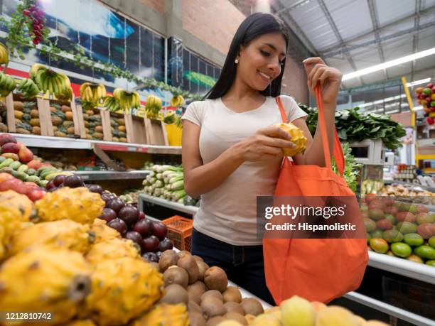 vrolijke vrouwelijke klant die een dragonfruit van vertoning kiest die het aan een herbruikbare zak toevoegt - marktplein stockfoto's en -beelden