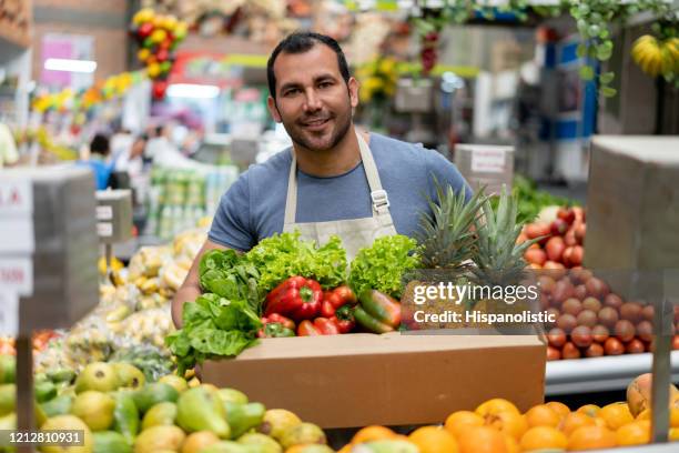 hombre guapo que trabaja en el mercado de un granjero sosteniendo una orden para el cliente en una caja de cartón mirando la cámara sonriendo - friendly salesman fotografías e imágenes de stock