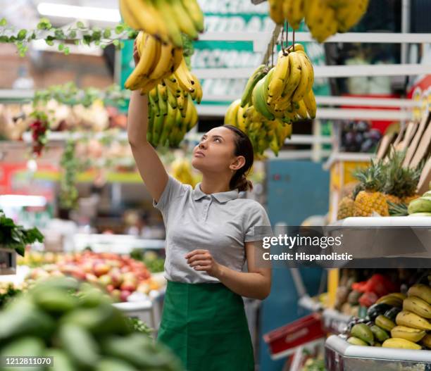 beautiful woman working at a vegetable and fruit kiosk arranging bananas - market square stock pictures, royalty-free photos & images