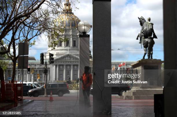 Worker power washes the sidewalk near San Francisco City Hall on March 16, 2020 in San Francisco, California. Public areas around the country are...