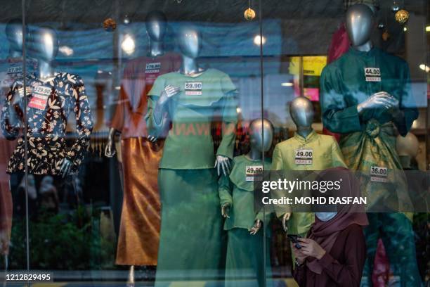 Woman wears a face mask as a preventive measure against the spread of the COVID-19 coronavirus as she browses her phone in front of a shop selling...
