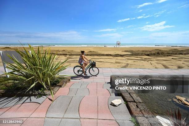 View taken on May 12, 2020 shows a woman riding a bicycle along a beach and the seafront in Jesolo, near Venice, northeastern Italy, during the...