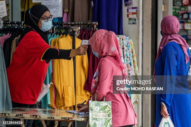 Vendor checks the temperature of a Muslim woman, as a preventive measure against the spread of the COVID-19 novel coronavirus, as she writes down her...