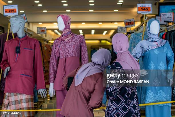 Muslim women look into a shop selling Malaysian cultural outfits called baju melayu and baju kurung ahead of the Eid al-Fitr festival, which marks...