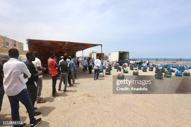 People wait in line to get cleaning materials and food aid provided by the United Nations High Commissioner for Refugees for irregular migrants and...