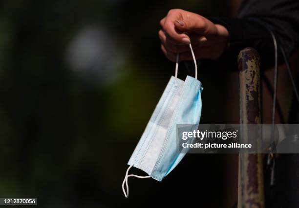 May 2020, Saxony, Bernsdorf: A woman holds her mouth guard in her hand in front of a bakery shop. Photo: Robert Michael/dpa-Zentralbild/dpa