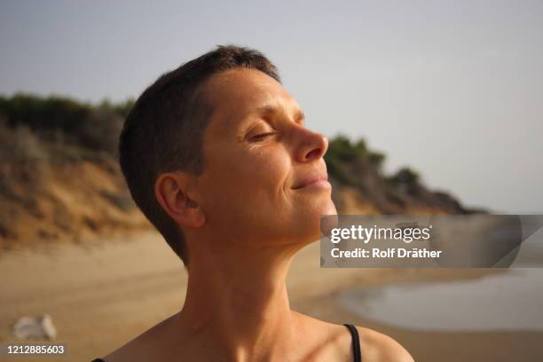 cabeza de una mujer con el pelo corto sonriendo y disfrutando del sol con los ojos cerrados en la playa - short hair fotografías e imágenes de stock