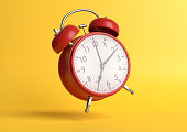 Red vintage alarm clock falling on the floor with bright yellow background in pastel colors