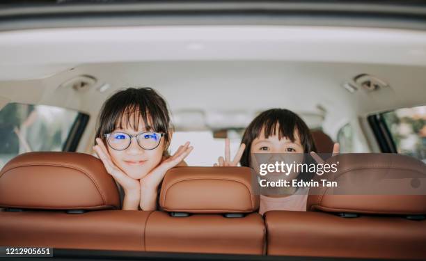 2 children looking at the camera from inside of a car smiling happily