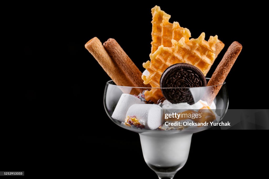 Tasty vanilla ice cream poured with salt caramel with marshmallows waffles and chocolate chip cookies on a black background isolated
