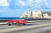 American red 1959 convertible vintage car on the promenade Malecon and in the background the Castillo de los Tres Reyes del Morro in Havana City Cuba - Serie Cuba Reportage