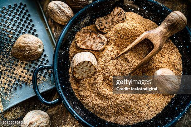 nutmeg seeds and ground nutmeg shot on rustic wooden table. - nutmeg stock pictures, royalty-free photos & images