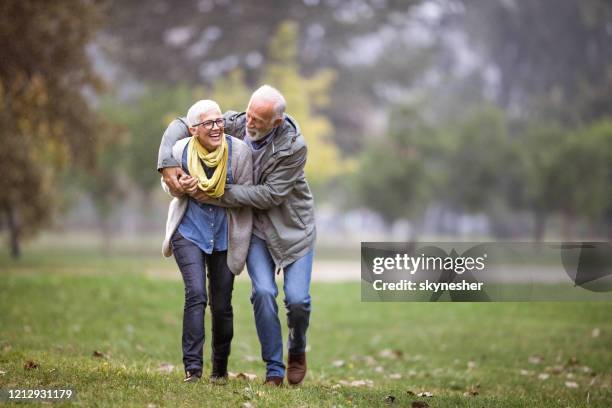 playful mature couple having fun during rainy day at the park. - mature couple winter outdoors stock pictures, royalty-free photos & images