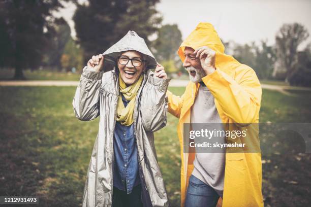 couples aînés heureux dans les imperméables pendant le jour pluvieux dans la nature. - se protéger de la pluie photos et images de collection