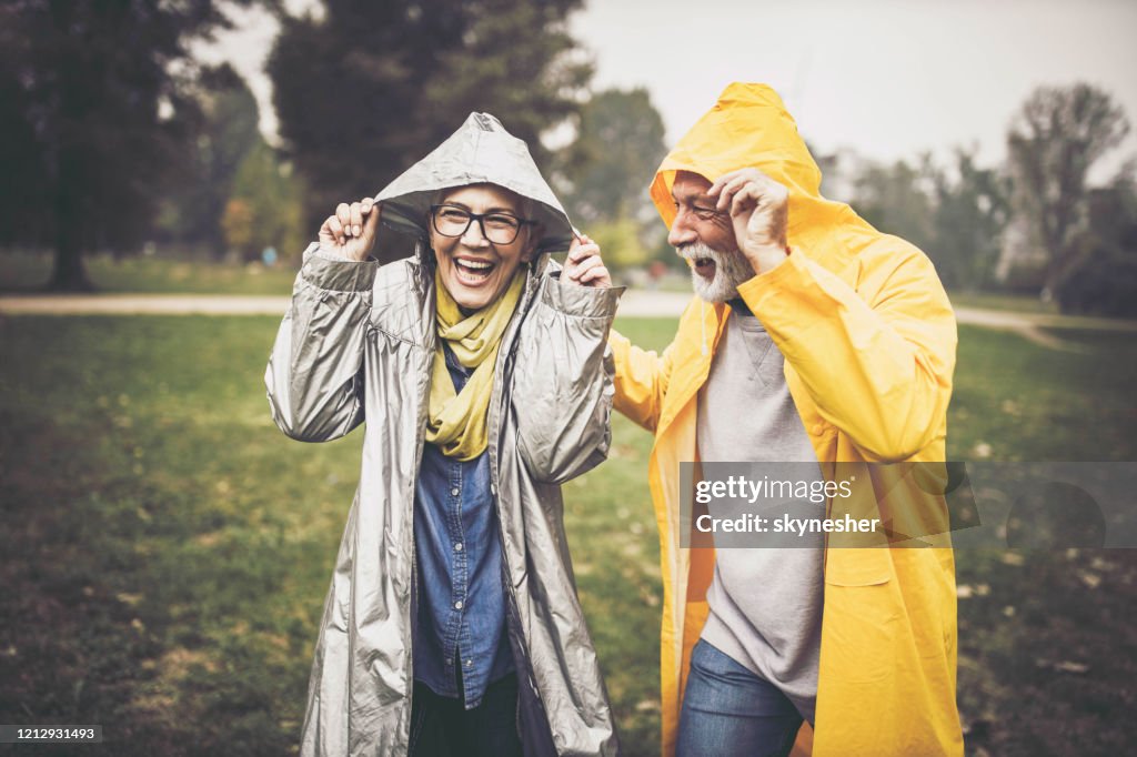 Felice coppia senior in impermeabili durante la giornata piovosa nella natura.