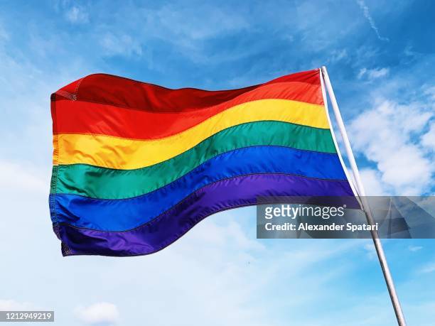 rainbow flag waving in the wind against blue sky - flagge stock-fotos und bilder