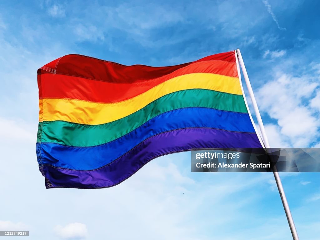 Rainbow flag waving in the wind against blue sky