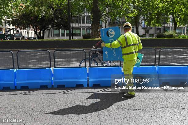 Worker puts the finishing touches to a pop-up cycle lane in Park Lane, London. Bollards have been added to the road to create segregation between...