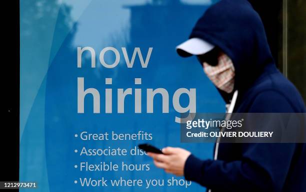 Man wearing a face mask walks past a sign "Now Hiring" in front of a store amid the coronavirus pandemic on May 14, 2020 in Arlington, Virginia. -...