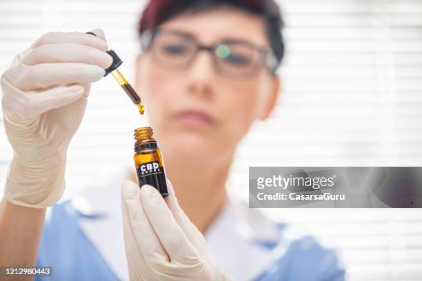 retrato de la mujer doctor sosteniendo gotas de aceite cbd - stock photo - cannabis oil fotografías e imágenes de stock